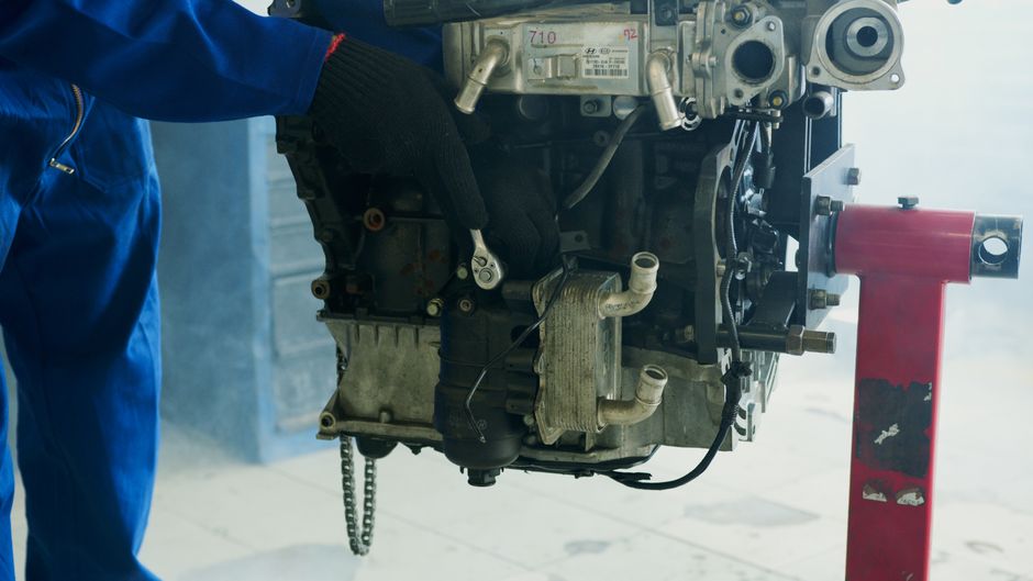 Mechanic wearing gloves uses a wrench to fix a car engine in a workshop.